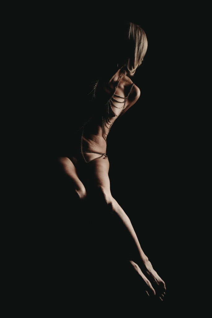 Mature blonde woman's silhouette looking away from the camera. She is nude except for a silver body chain that adorns her entire body. Featured in the blog post "Boudoir Inspo: Nudescape or Bodyscape Photography" nudescape, beautiful boudoir, boudoir style, imagery style, Colorado boudoir photographer, Body positive boudoir, Body Image, inspiration, style, black and white imagery, composition. Picture by Embodied Art Boudoir.