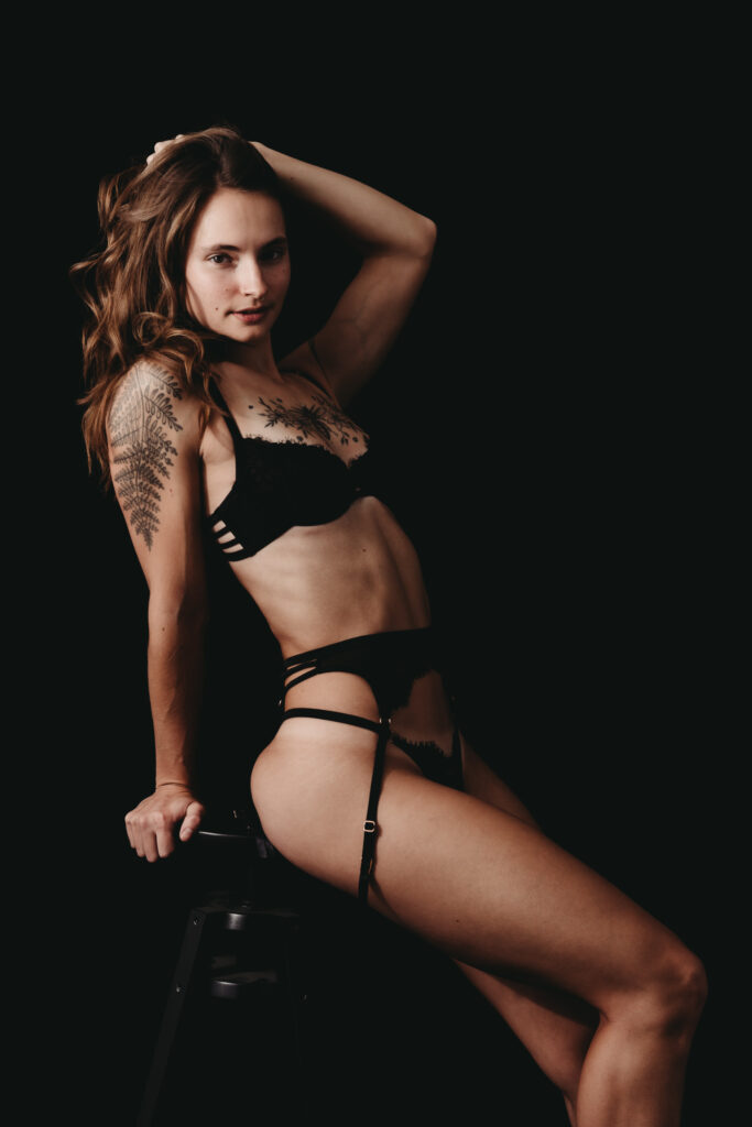 A petite brunette Girl wearing all black and garter sitting on a stool. Featured in the Blog Boudoir Outfit Ideas & Inspiration for 2024: How to Pick the Perfect Boudoir Look. Boudoir photography, colorado boudoir, denver boudoir, boulder boudoir, colorado springs boudoir, boudoir ideas, boudoir poses, boudoir inspiration, boudoir outfits, curvy boudoir, plus size lingerie, lingerie, photoshoot outfits, flattering outfits, curvy lingerie, lingerie look, lingerielook photoshoot, lingerie outfit, lingerie outfit bedroom, lingerie party, outfit ideas. image by Embodied Art Boudoir. 