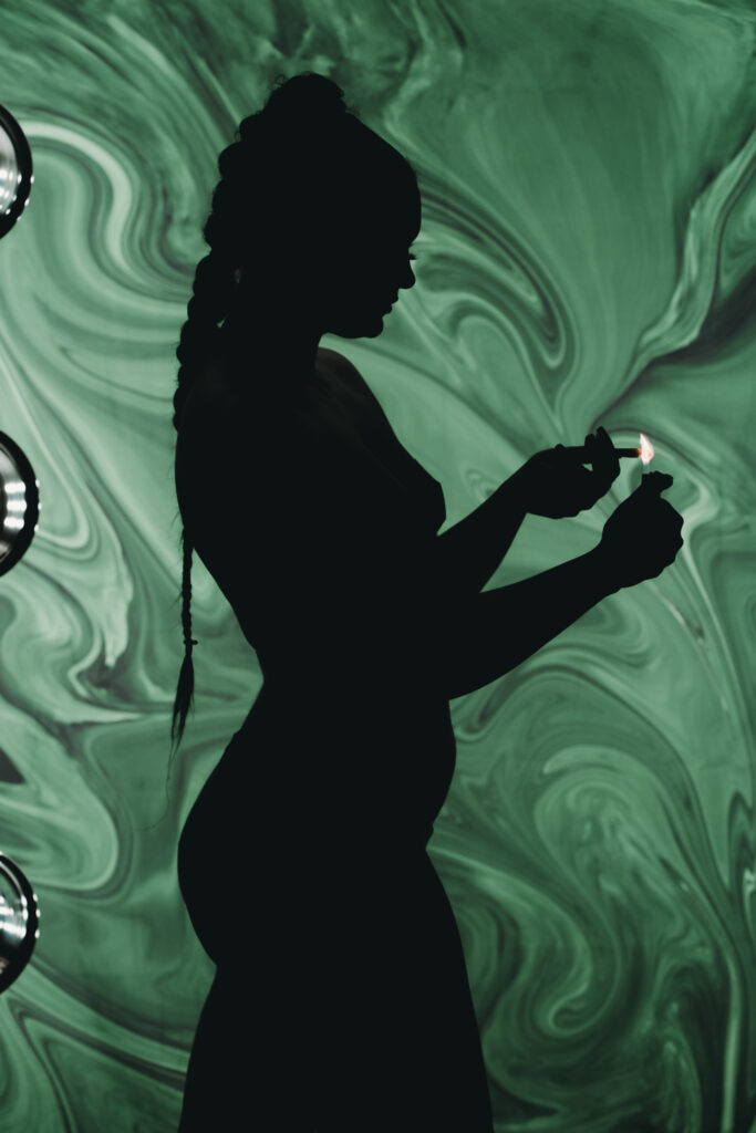 Mysterious silhoutte of a womans profile with a high braid as she lights a joint in front of a trippy green background. . Featured in the blog "Outfit & Prop Ideas For The Green Room: Boudoir 420 Photoshoot." boudoir, sensual, sexy, playful, flirty, provocative, daring, confident, edgy, creative, unique, expressive, intimate, vibrant, lush, dramatic, whimsical, mysterious, artistic, stylish, bold, fun, liberating, empowering, seductive, luxurious, unapologetic, radiant, magnetic, alluring, captivating, enticing, glamorous, seductive, spirited, mischievous, charismatic, empowering, personal, transformative, celebratory, indulgent, immersive, photogenic. Photo by Embodied Art Boudoir