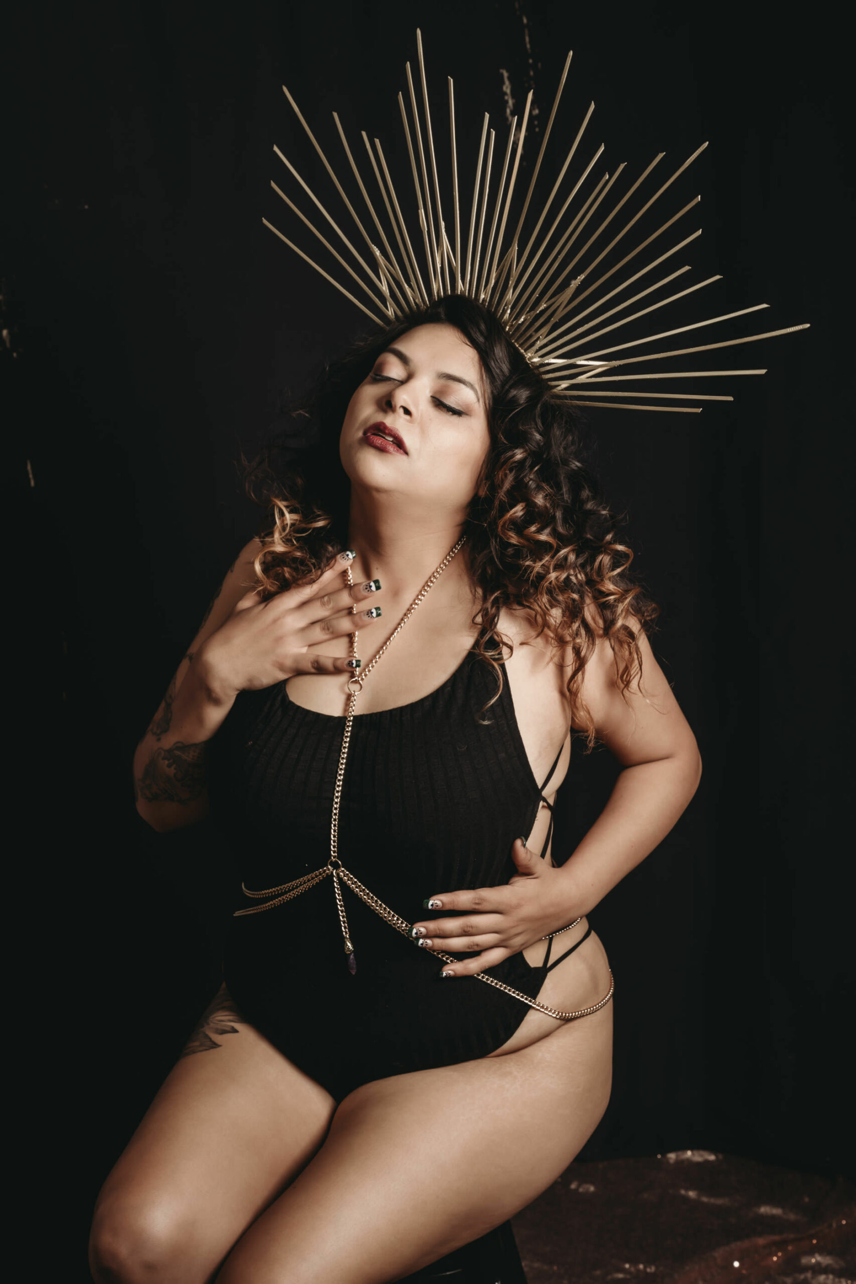 Woman sitting in a black body suit and gold body chain and crown. Photo by Embodied Art Boudoir, boudoir posing, boudoir inspiration, plus size photography, plus size boudoir, plus size glamour, plus size posing, plus size outfits, fat boudoir, fat empowerment, body positivity, fat positive, body positive, body confidence, body empowerment, haes, colorado boudoir, denver boudoir.