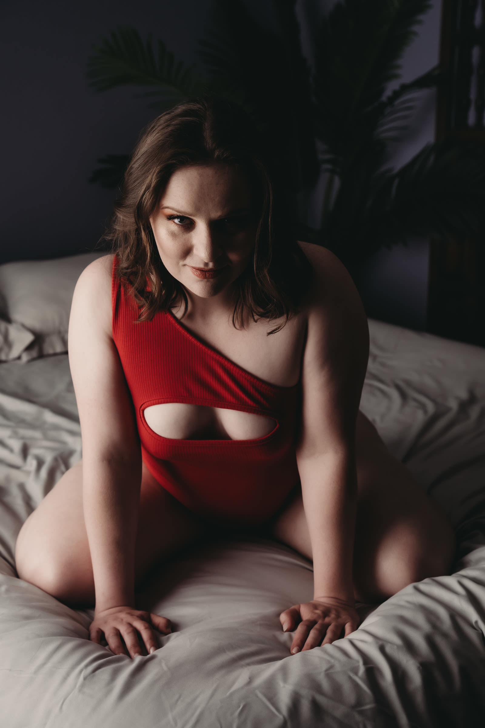 Woman kneeling on bed, looking at camera wearing red bodysuit. Photo by Embodied Art Boudoir, boudoir posing, boudoir inspiration, plus size photography, plus size boudoir, plus size glamour, plus size posing, plus size outfits, fat boudoir, fat empowerment, body positivity, fat positive, body positive, body confidence, body empowerment, haes, colorado boudoir, denver boudoir
