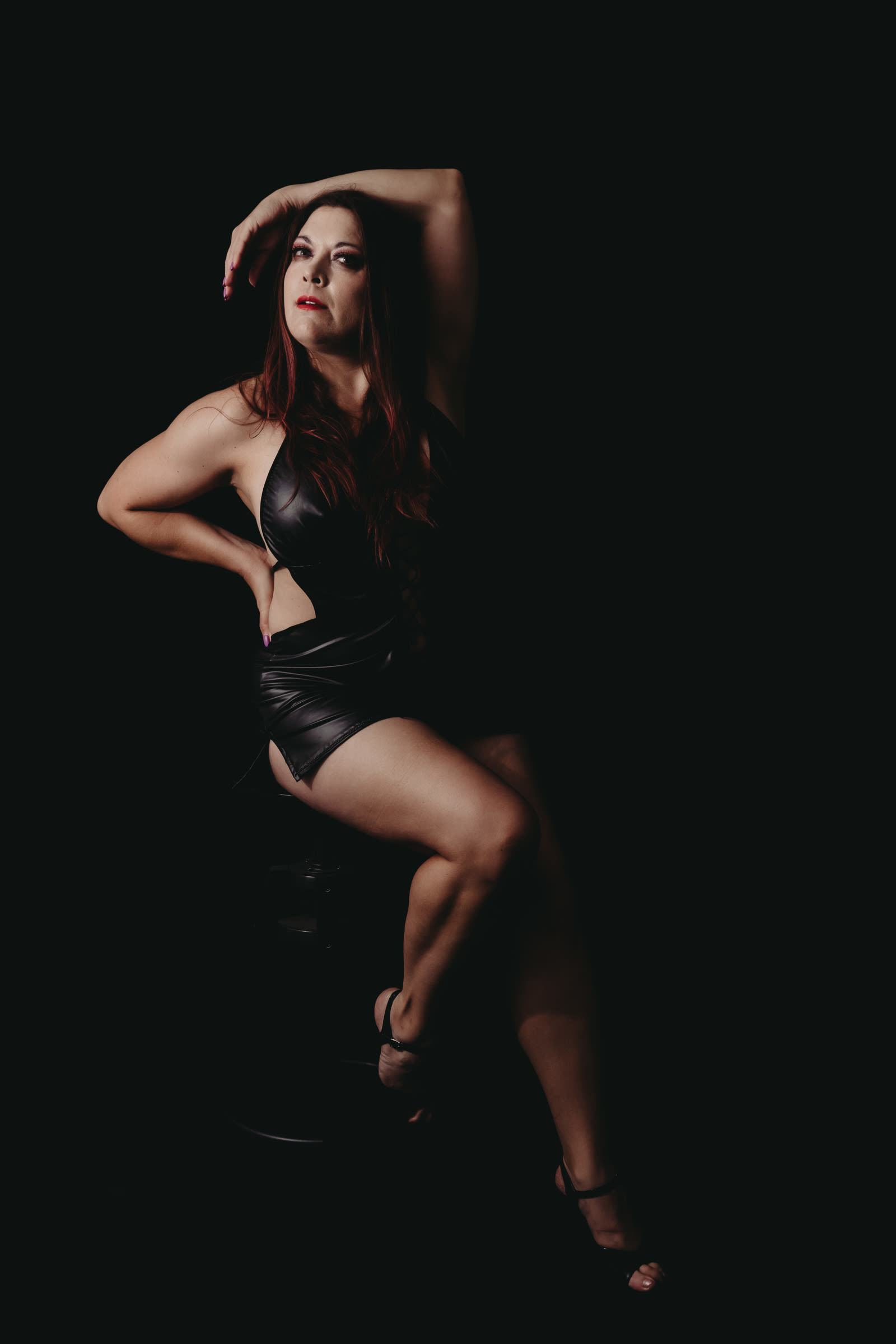 Woman sitting on stool wearing black leather dress and black heels. Photo by Embodied Art Boudoir, boudoir posing, boudoir inspiration, plus size photography, plus size boudoir, plus size glamour, plus size posing, plus size outfits, fat boudoir, fat empowerment, body positivity, fat positive, body positive, body confidence, body empowerment, haes, colorado boudoir, denver boudoir