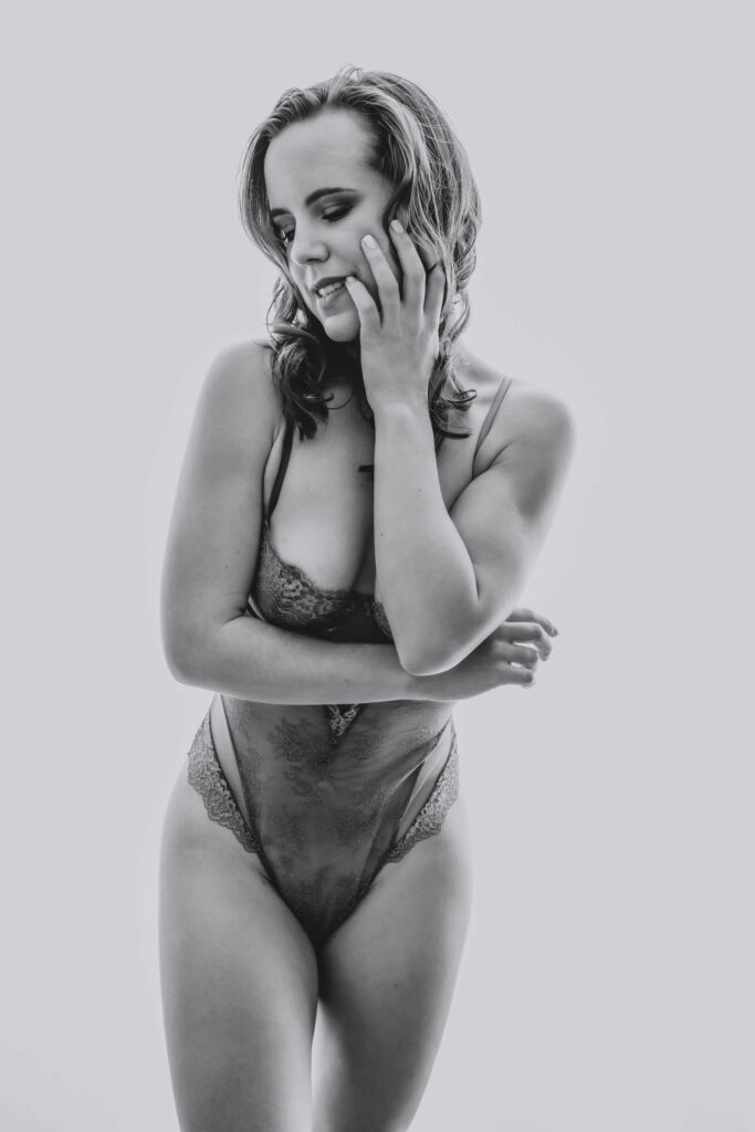 Black and white photo of a blonde woman standing wearing a lacy body suit as she looks to the side showcasing her side profile. Featured in the blog "High Key Boudoir Photography Style". high key photography, high key, bright photohraphy, sensual photography, sensual boudoir, colorado boudoir, denver boudoir, boulder boudoir, colorado springs boudoir, boudoir ideas, boudoir poses, boudoir inspiration, photography inspiration, romantic boudoir, bridal boudoir, female empowerment, female photographer. Photo by Embodied Art Boudoir.