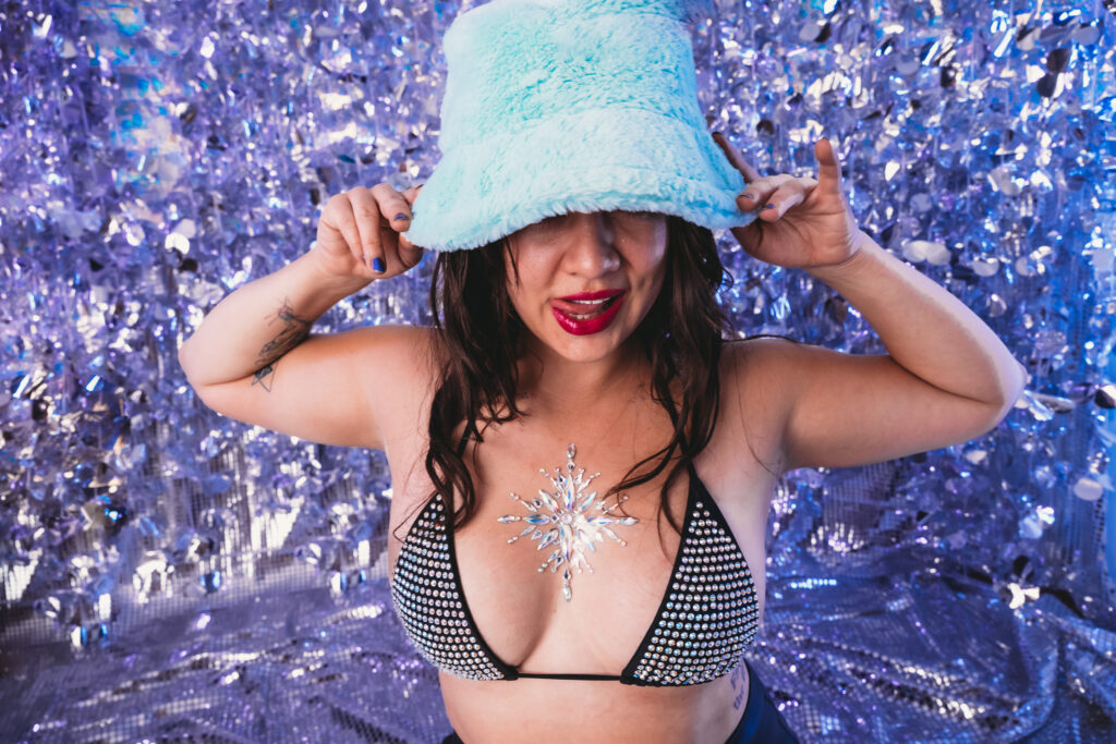 Woman standing in front of bright disco background, wearing a sparkling bra and a fuzzy blue bucket hat. Photo by Embodied Art Boudoir. Preparation, get ready, prep for your boudoir shoot, plan for your boudoir photoshoot, organized, boudoir inspiration, boudoir ideas, colorado boudoir, denver boudoir, boulder boudoir, colorado springs boudoir, female photographer, planner, boudoir fun, boudoir is for everyone