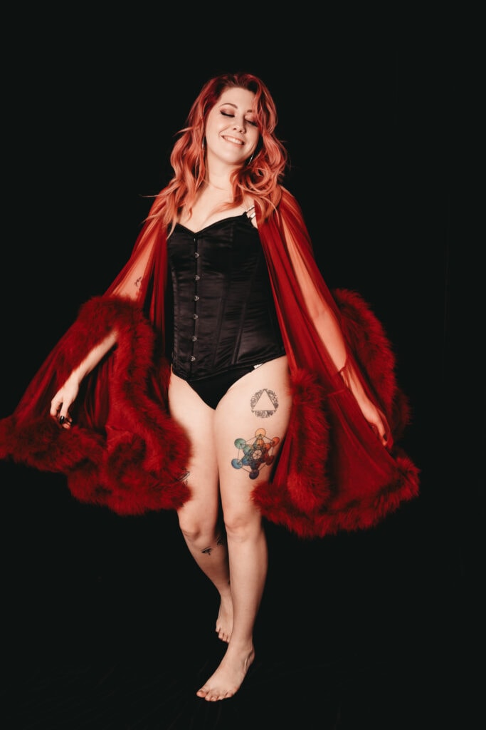 Red hair woman wearing a black corset and a frilly red robe. Featured in the blog, "Best Accessories For Your Boudoir Photoshoot" Accessories, boudoir outfits, boudoir style, boudoir looks, accessorise, sheets, jewellery, scarf, sheet, creative outfits, sexy look, confidence, boudoir photoshoot, classy photography, sensual photography, sensual boudoir, colorado boudoir, denver boudoir, boulder boudoir, colorado springs boudoir, boudoir ideas. Photo by Embodied Art Boudoir.
