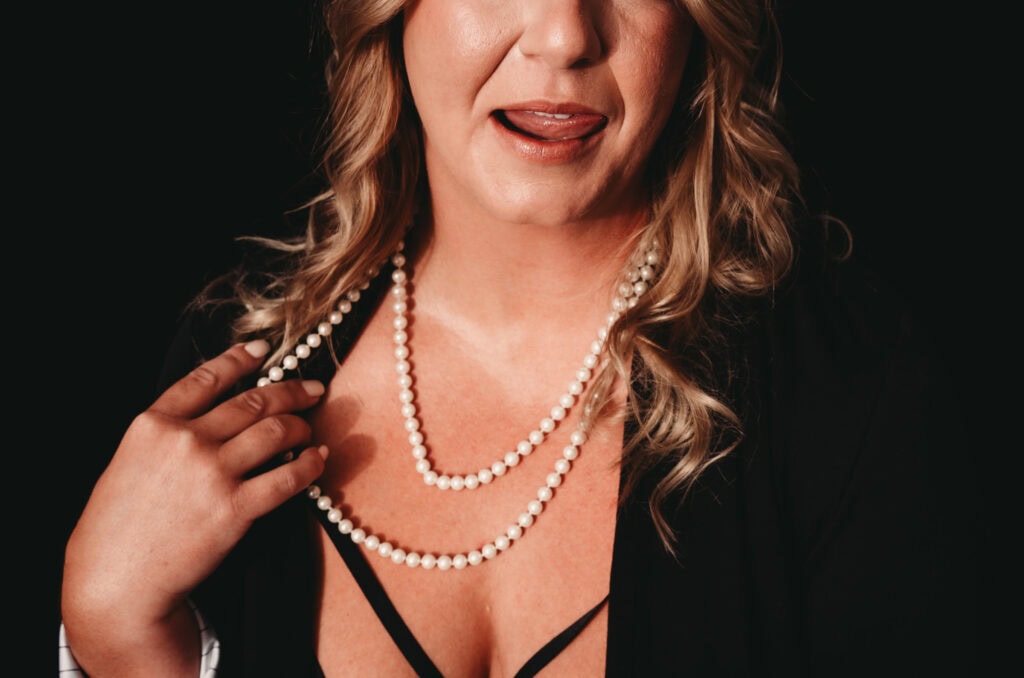 Mature blonde woman posing up close showcasing her red lipstick, and pearl necklace. Featured in the blog, "Best Accessories For Your Boudoir Photoshoot" Accessories, boudoir outfits, boudoir style, boudoir looks, accessorise, sheets, jewellery, scarf, sheet, creative outfits, sexy look, confidence, boudoir photoshoot, classy photography, sensual photography, sensual boudoir, colorado boudoir, denver boudoir, boulder boudoir, colorado springs boudoir, boudoir ideas. Photography by Embodied Art Boudoir.