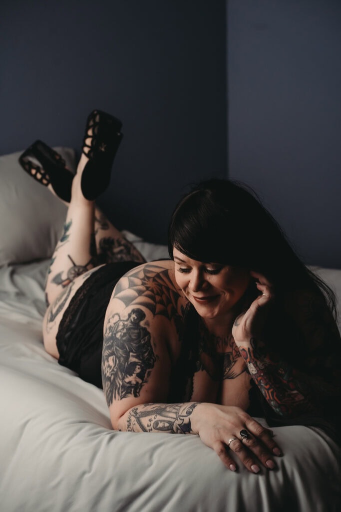 Woman with long black hair and tattoos lying on bed wearing black panties and black high heels. hoto by Embodied Art Boudoir. Accessories, boudoir outfits, boudoir style, boudoir looks, accessorise, sheets, jewellery, scarf, sheet, creative outfits, sexy look, confidence, boudoir photoshoot, classy photography, sensual photography, sensual boudoir, colorado boudoir, denver boudoir, boulder boudoir, colorado springs boudoir, boudoir ideas