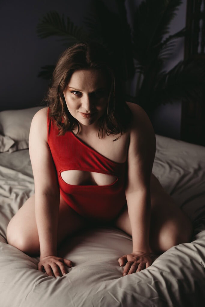 Woman wearing a red body suit sitting on her knees on bed. Photo by Embodied Art Boudoir. Embrace sensuality, sensual, wellness, connection, embodied, desires, five senses, connected, imperfectly perfect, body journey, body love, colorado boudoir, denver boudoir, boulder boudoir, colorado springs boudoir, boudoir ideas, boudoir poses, boudoir inspiration, photography inspiration