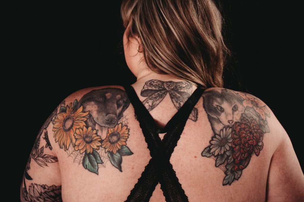 Plus sized blonde woman hair and back standing in front of a black background wearing a black bra and showcasing her tattoos. Featured in the blog, "The Connection Between Mindfulness And Self-Expression In Boudoir Photography" Mindful, mindfulness, brain and body, brain body connection, yoga, pause, live in the moment, intention, journal, self expression, confidence, express yourself, embodied, boudoir photos, colorado boudoir, denver boudoir, boulder boudoir, colorado springs boudoir. Photography by Embodied Art Boudoir.