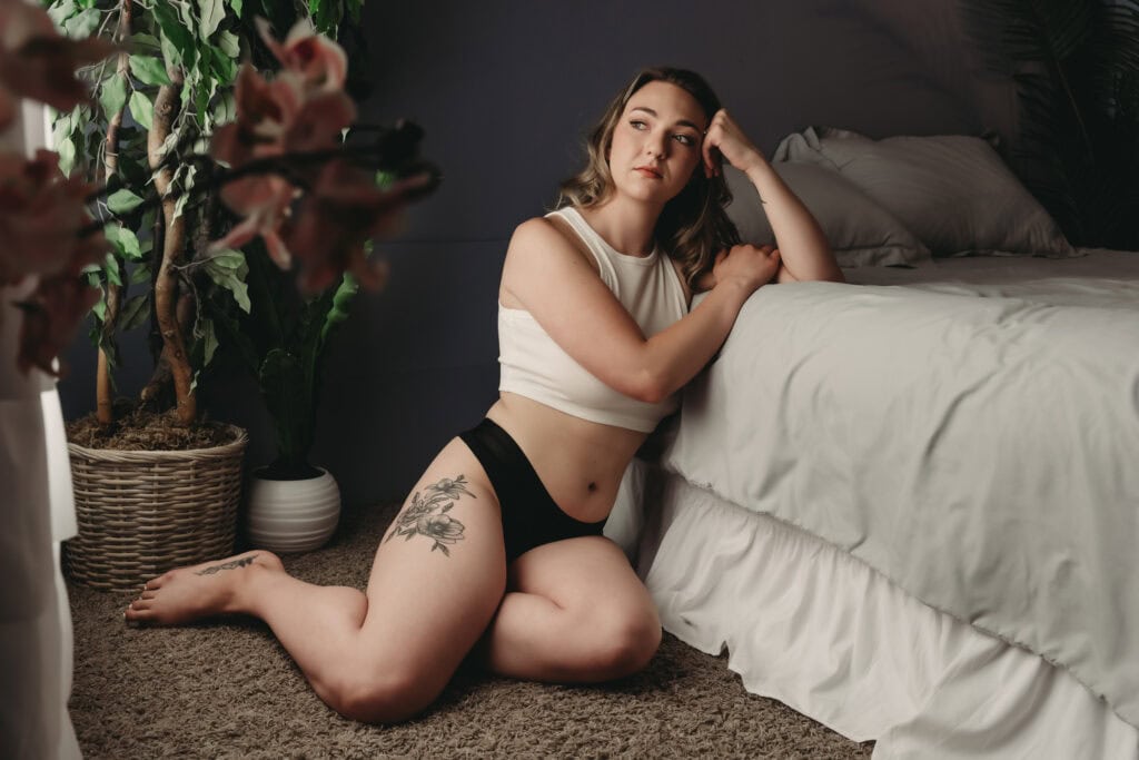 Woman leaning on wearing a black panties and a white tank top, looking pensive. Photo by Embodied Art Boudoir. Celebrate, journey, growth, self-acceptance, self-love, body neutrality, embodiment, confidence boost, boudoir photography, photoshoot, boudoir, colorado boudoir, denver boudoir, boulder boudoir, colorado springs boudoir