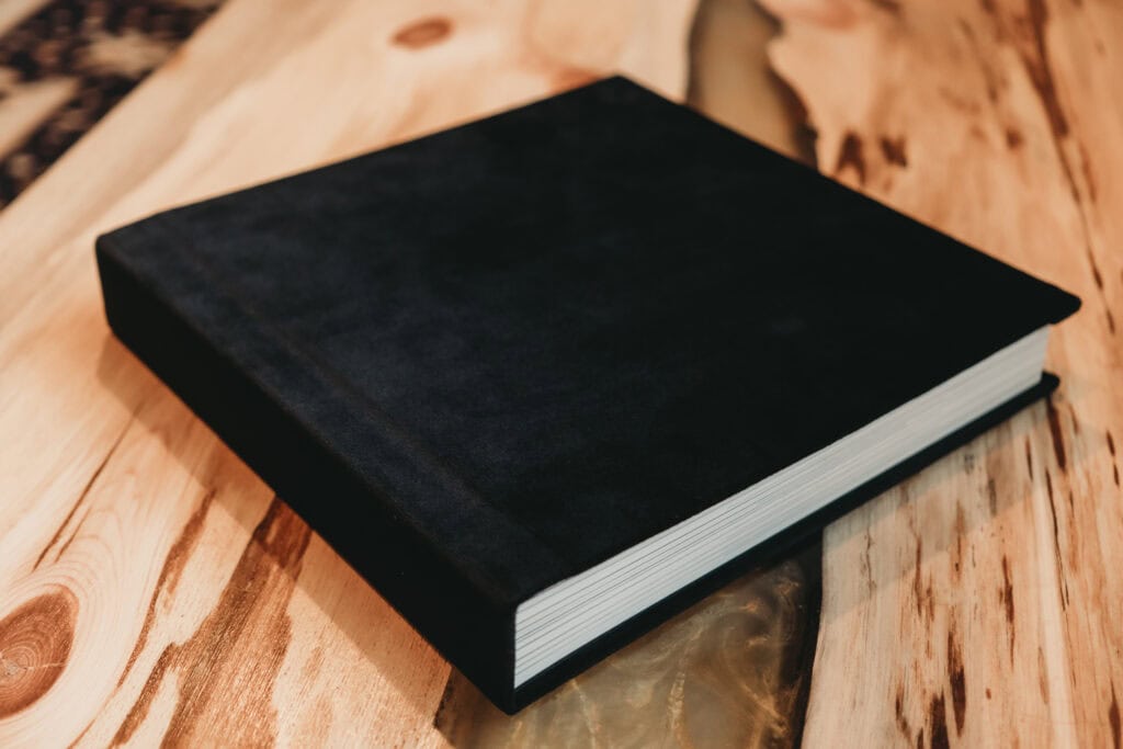 The image is featuring a thick black velvet photo album which is placed on top of a wooden table. Featured on Denver Boudoir Photography - Body Positive Boudoir for 2025. Photo by Embodied Art Boudoir. Denver boudoir photographer, Colorado boudoir photographer, Colorado boudoir photography, boudoir photoshoot, boudoir artwork, body confidence
