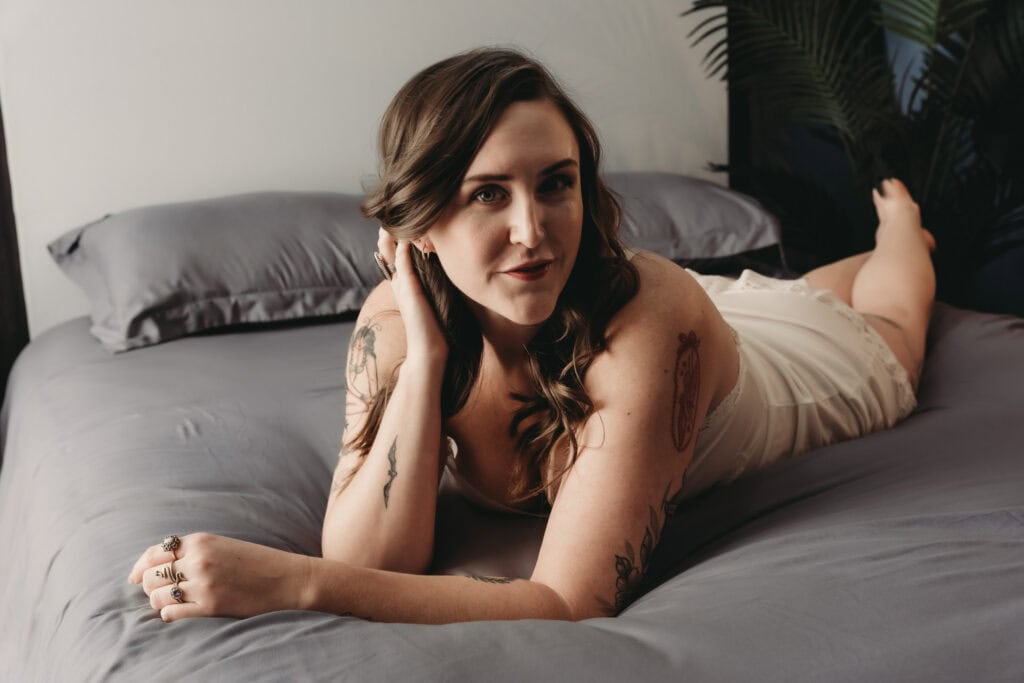 Tattooed woman lying on bed, boudoir photography, natural light, Denver, Embodied Art Boudoir.