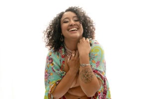 A woman smiling confidently, wearing colorful bohemian attire and jewelry.