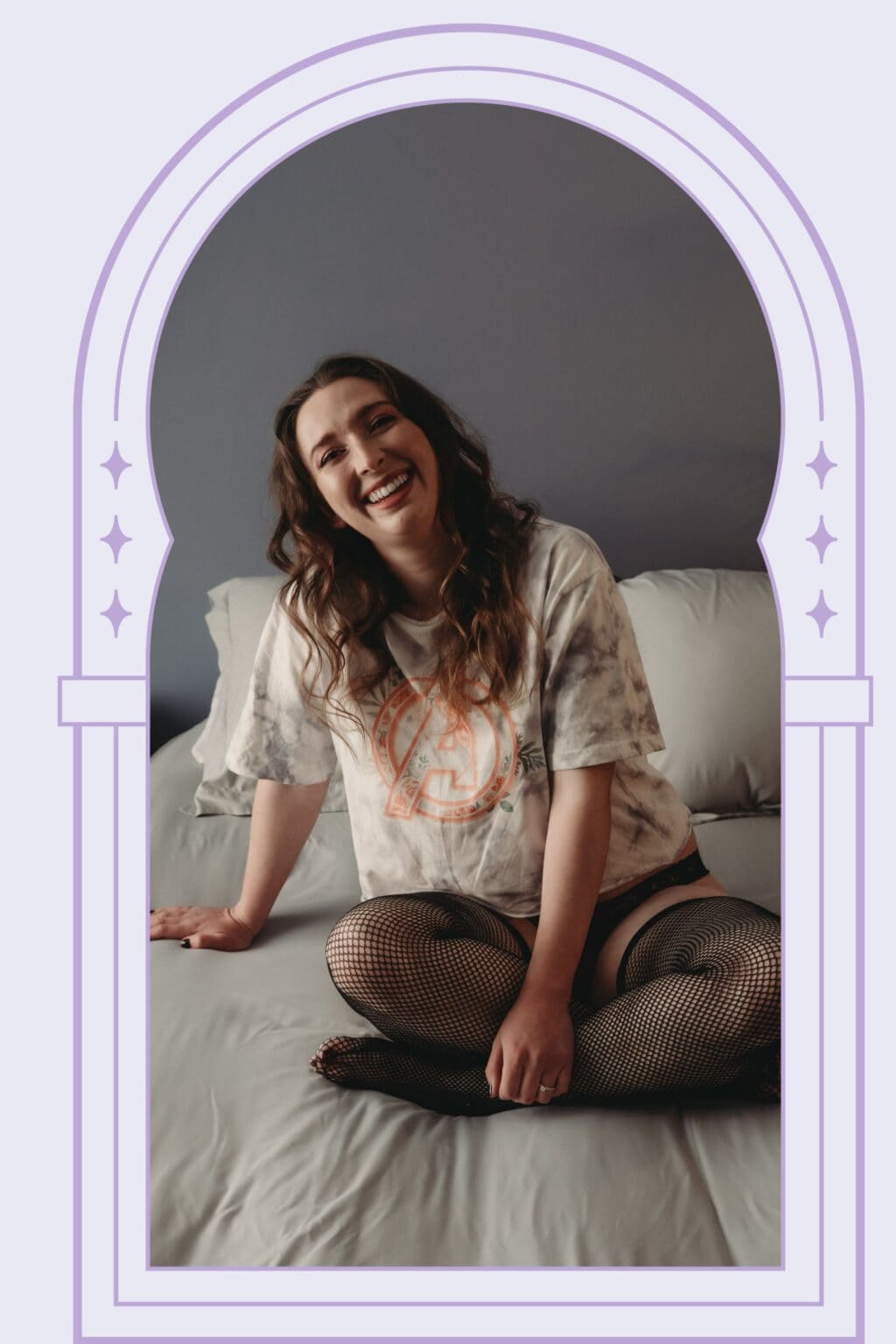 A woman smiling and sitting on a bed in casual attire with fishnet stockings.